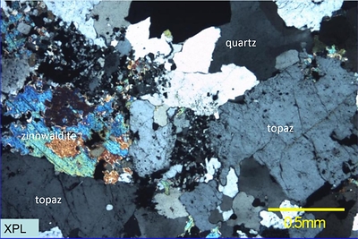 Figure 5: Thin section photographs of sample GM10402a taken with polarized light (crossed polars). Coloured grains are zinnwaldite, large ragged grey grains are quartz, smaller dark grains are topaz. Note that this photo is not intended to be representative of broader mineralization on the Project. (CNW Group/TinOne Resources Corp.)