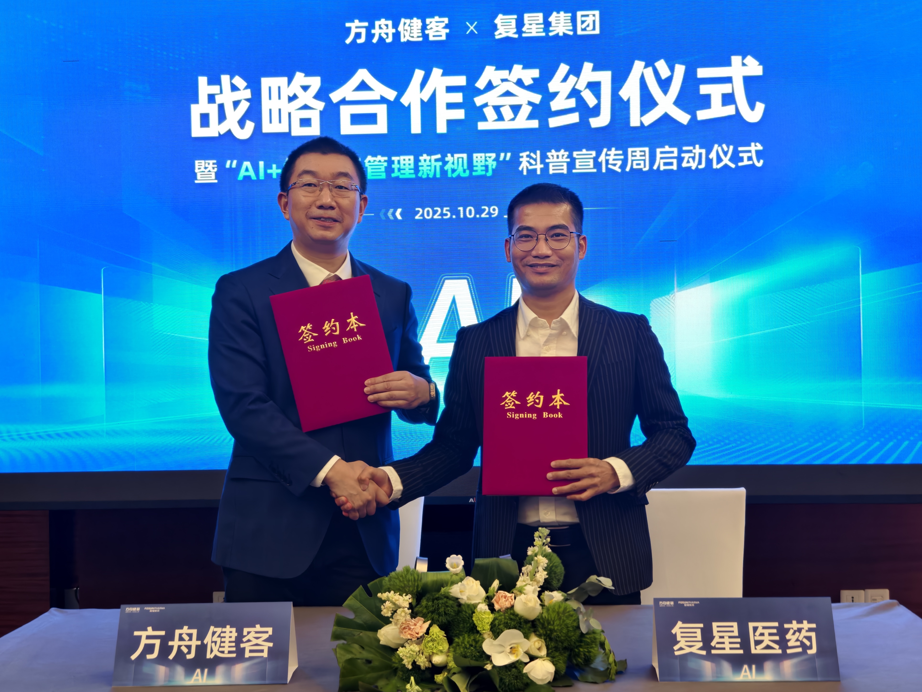 wo men in suits shake hands while holding red signing books, at a strategic cooperation signing ceremony